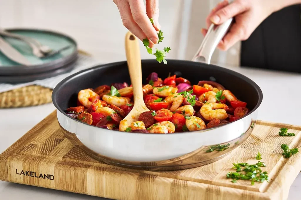 Lakeland Stainless Steel Non-Stick Frying Pan 28cm on a worktop frying vegetables